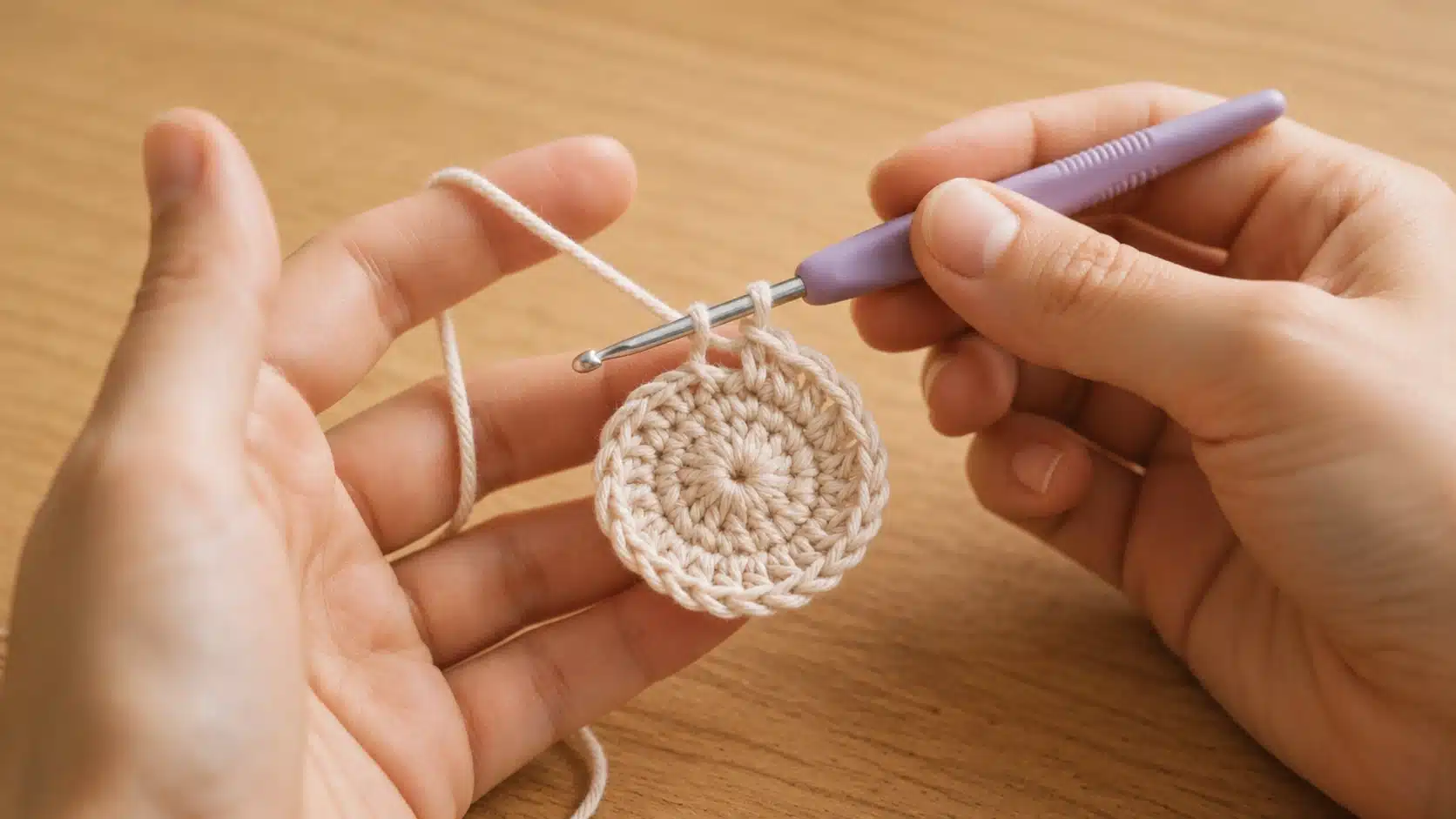 Hands holding a beige crochet circle with a yellow handled hook and working yarn stretched across the fingers gently