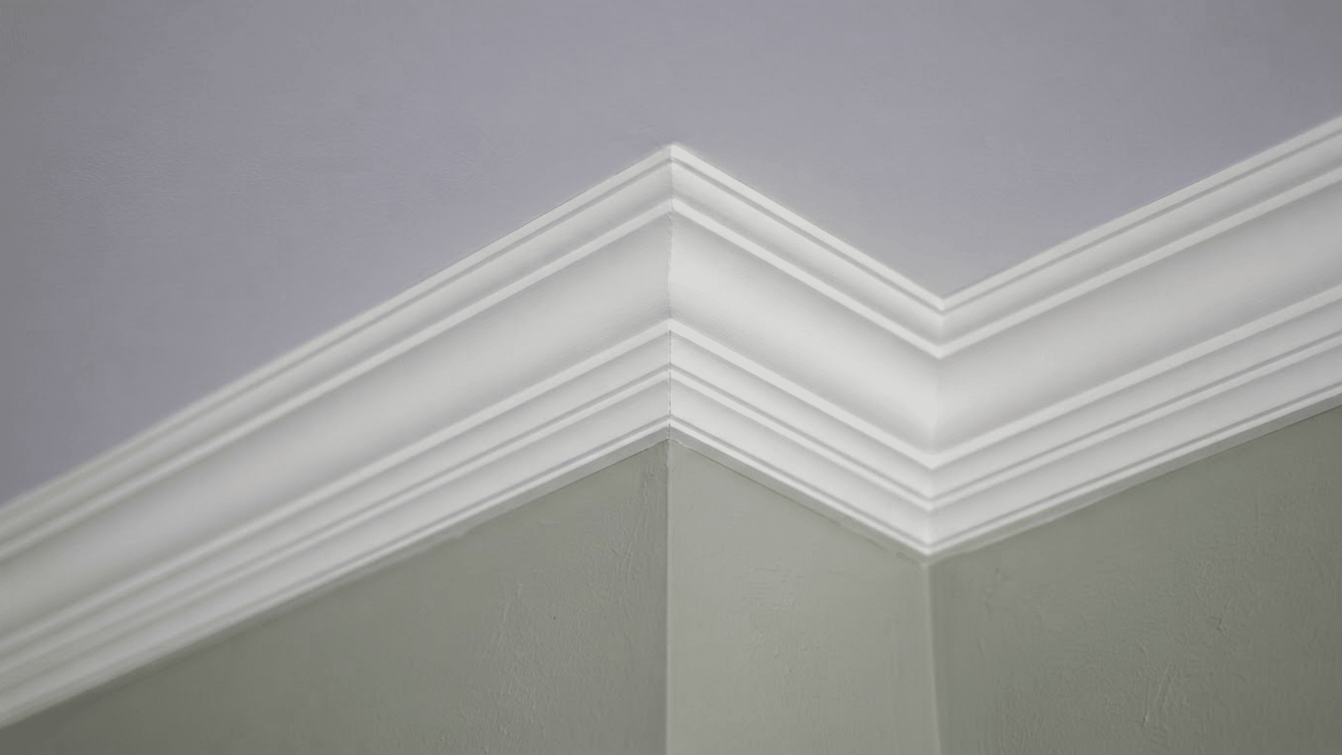 stepped crown molding with layered white lines meeting at an interior corner above green walls