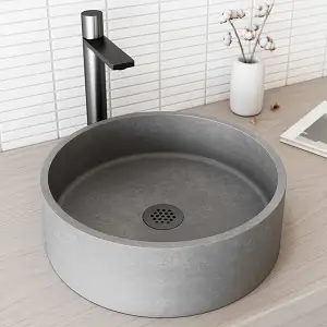 Circular stone sink with black faucet on light wooden countertop in minimalist bathroom