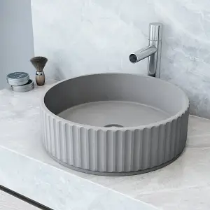 Round gray concrete sink with ridged sides on marble countertop in modern bathroom