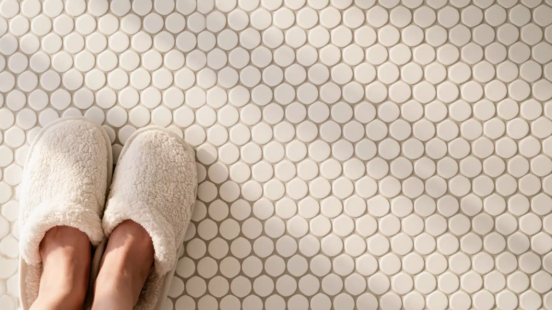 Overhead view of feet in slippers on a white penny round mosaic tile floor