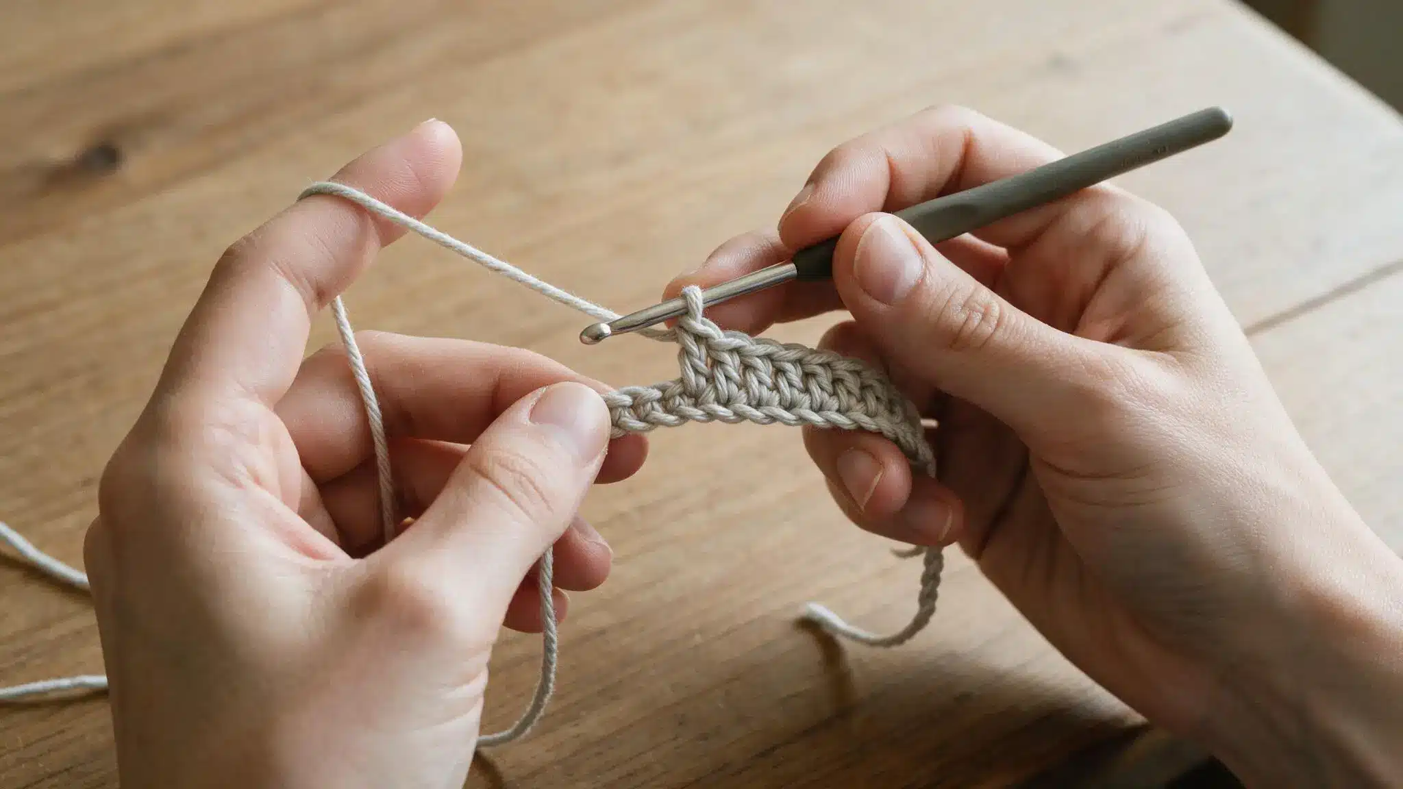 Hands using a crochet hook to work the first row of stitches into a crochet chain