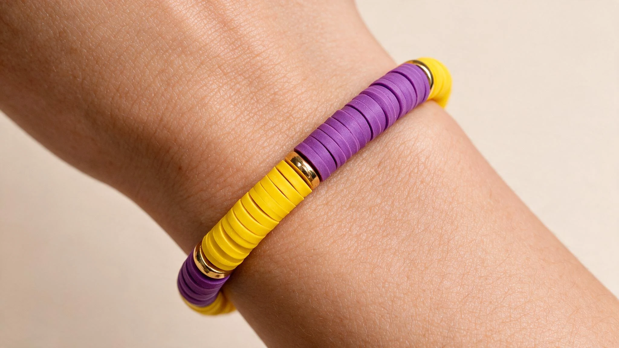 A woman's hand holds a vibrant purple and yellow bracelet, showcasing bold color blocks in a stylish design.