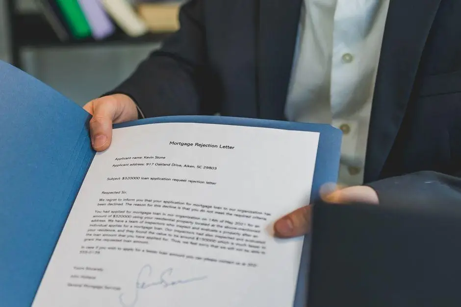 Person holding formal letter in blue folder, wearing dark suit in office setting