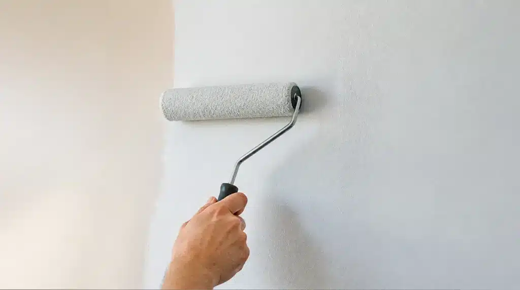 Person using a paint roller to apply a fresh coat of white paint to an interior wall