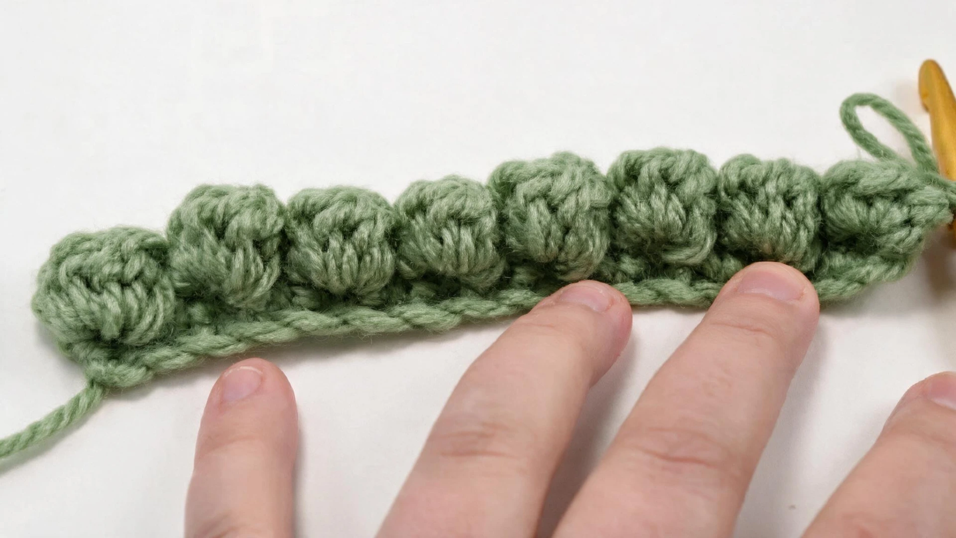 Row of evenly spaced green bobble stitches worked across the crochet foundation.