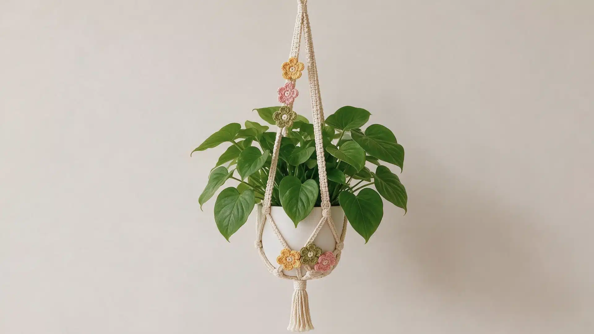 Cream floral with yellow pink and sage crochet flowers holding a leafy green plant in a white pot.