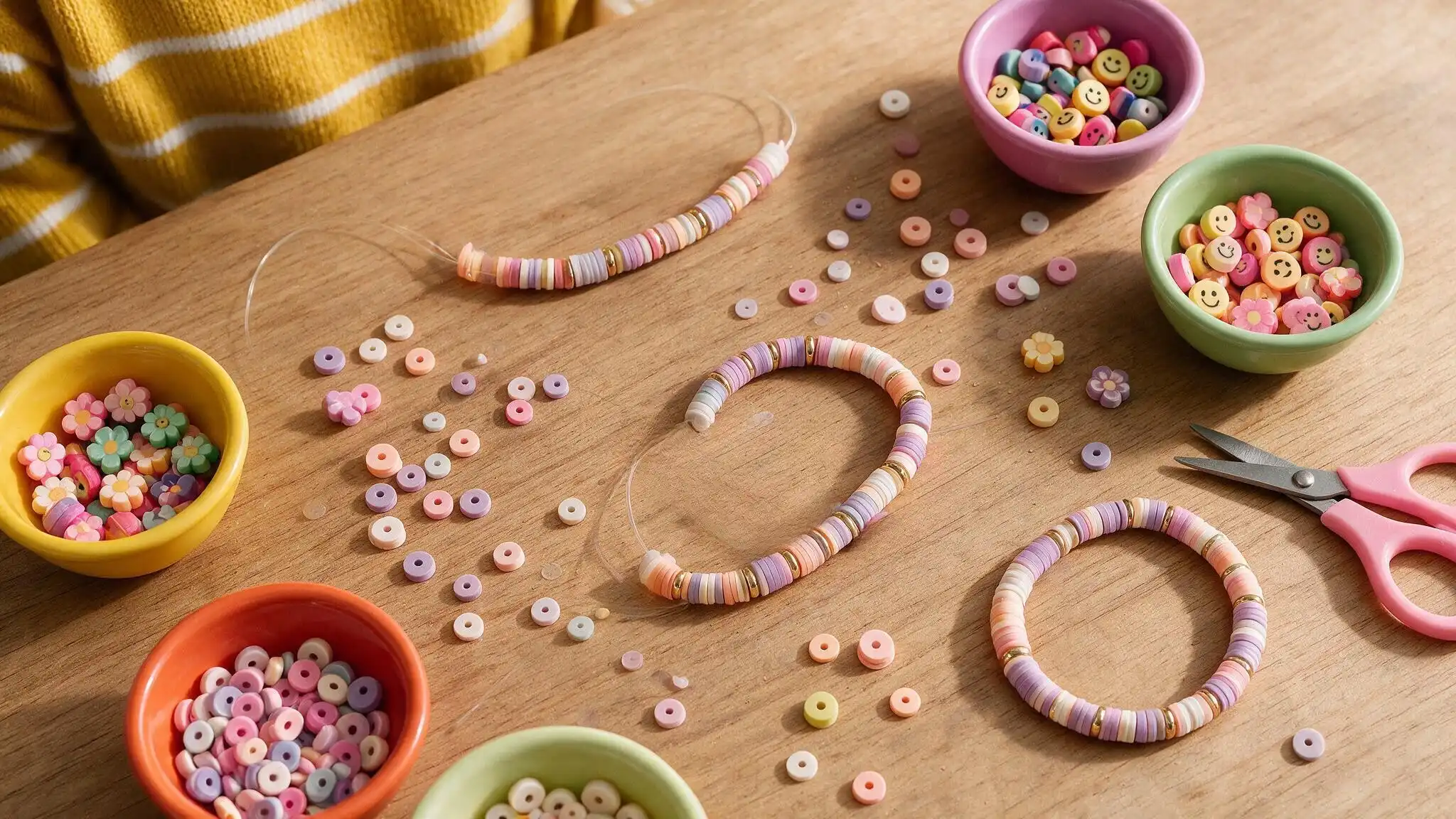 A table displaying colorful candy beads and scissors, set up for making a clay bead bracelet.