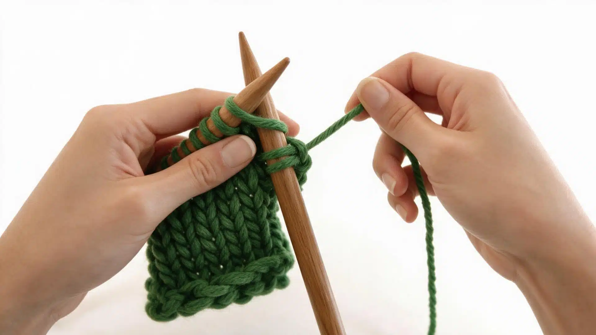 Hands knitting the next stitch with green yarn to continue the cast off sequence.