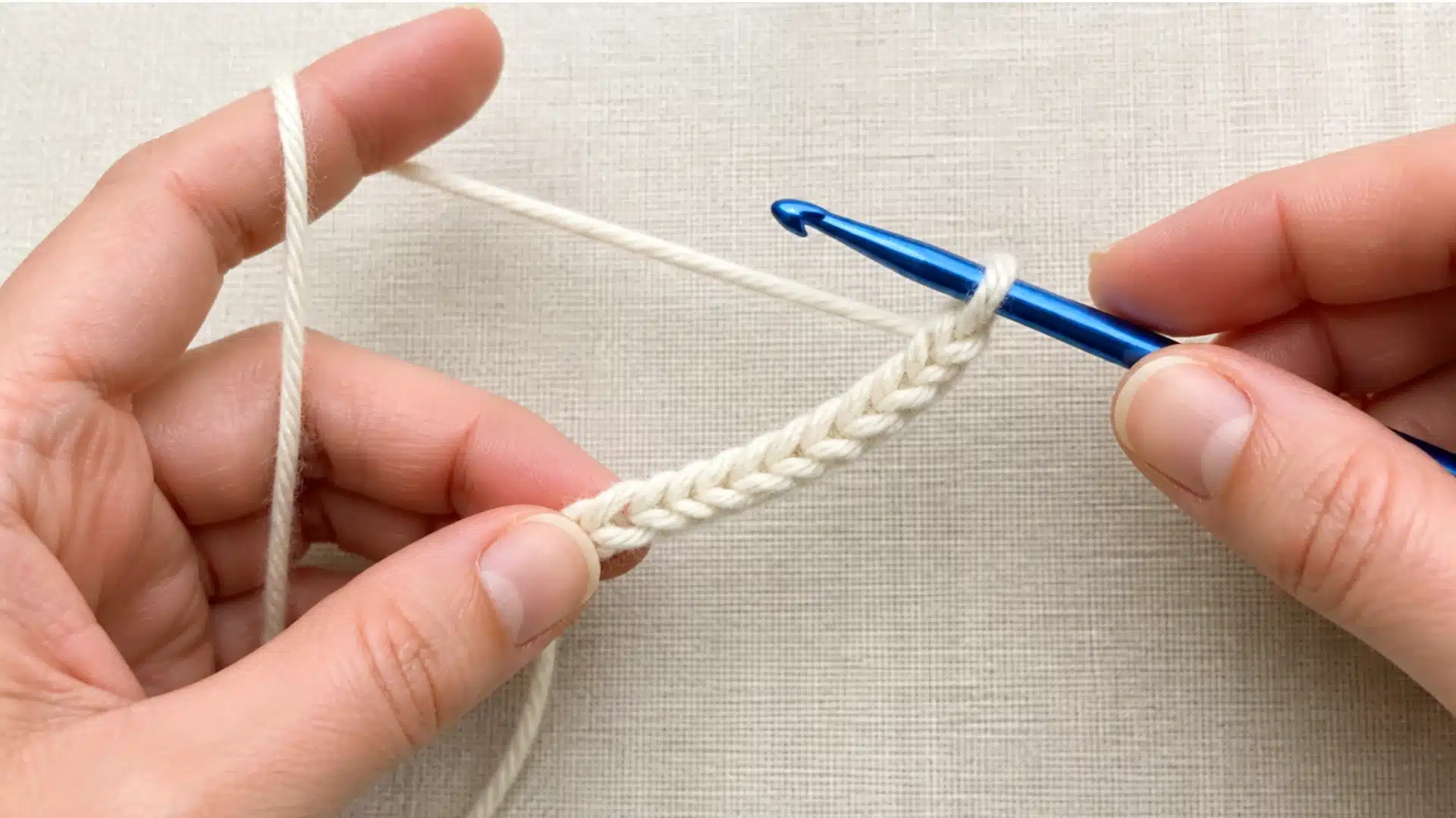 A person holds a crochet hook, demonstrating the technique for creating a foundation chain in knitting.