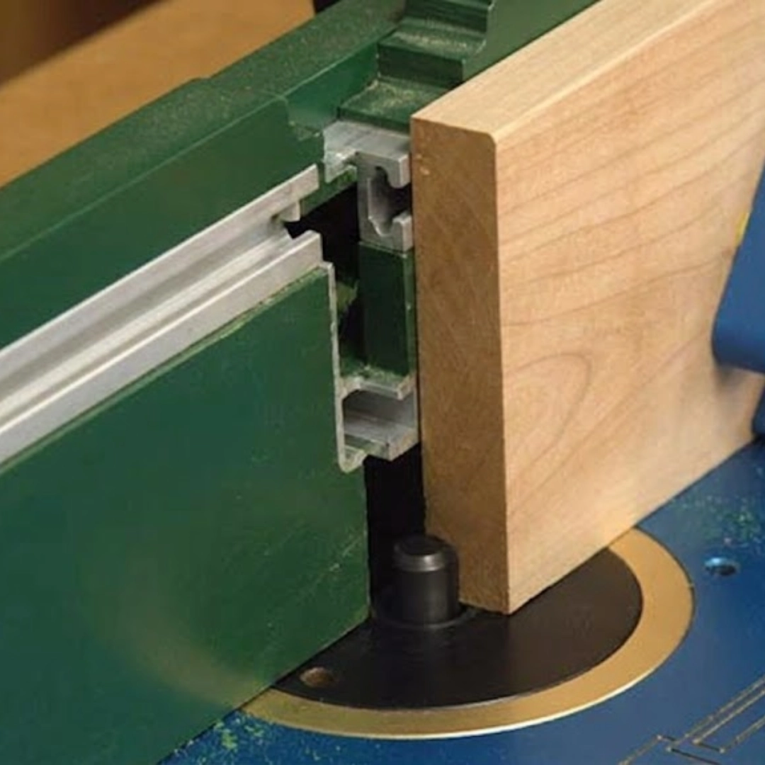 Close-up of a wood board against a router table fence while a straight bit cuts a clean rabbet along the board's edge.