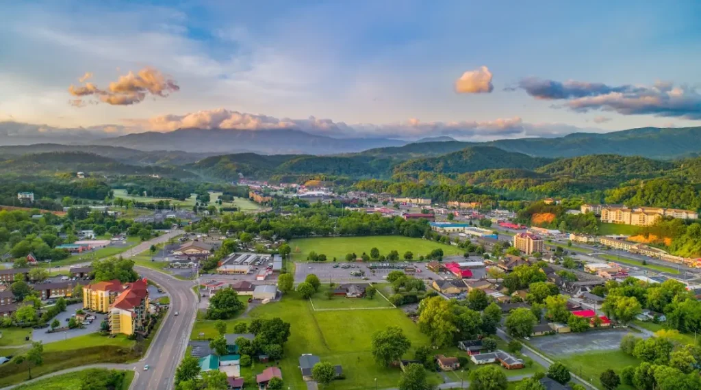 Aerial view of town nestled among lush green hills and mountains under colorful clouds