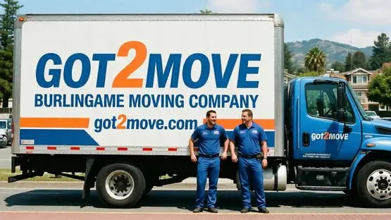 Two movers in blue uniforms standing beside Got2Move truck outdoors