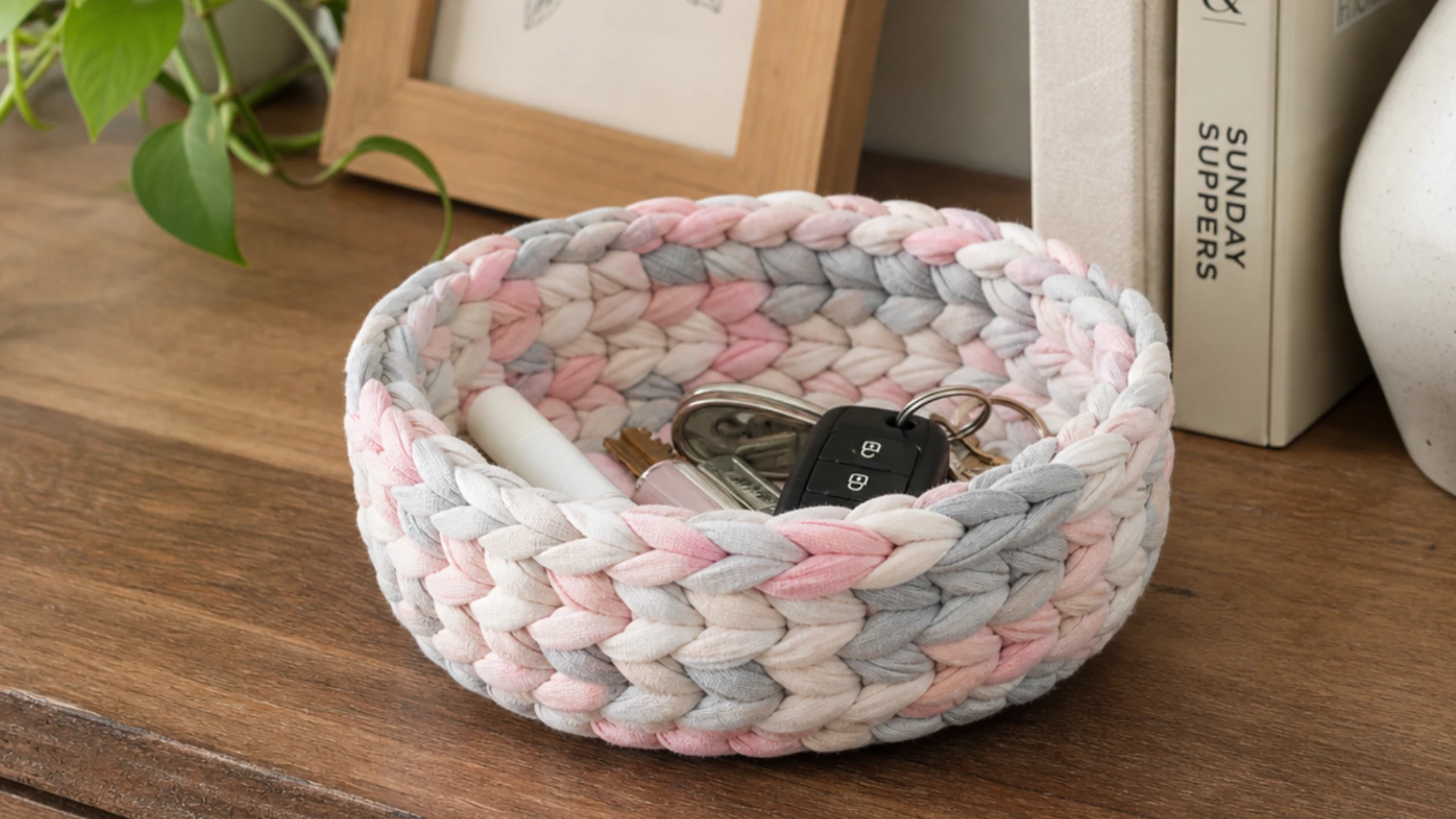 Braided fabric bowl in soft pink gray and white holding keys and small items on a wooden table