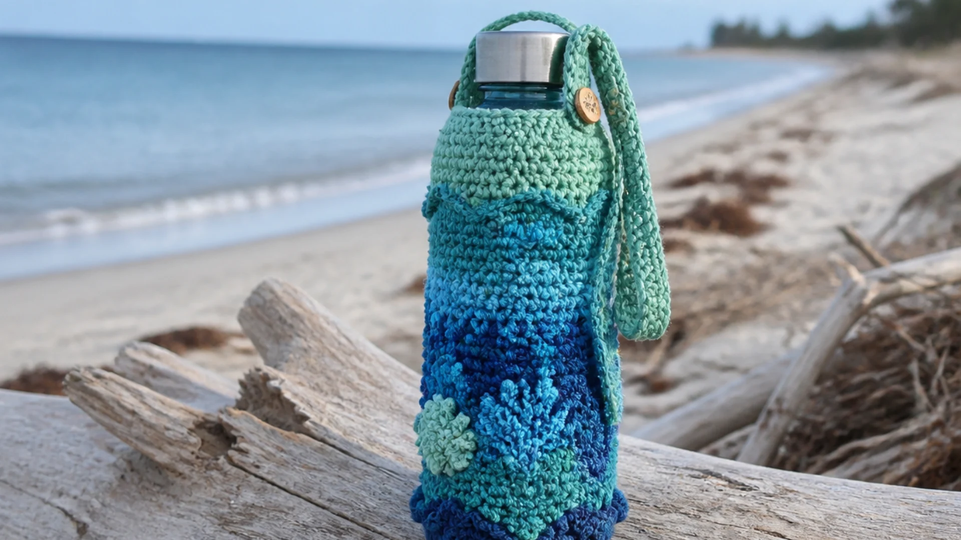 Blue and teal ocean inspired <echighlighted><echighlighted>crochet water bottle holder</echighlighted></echighlighted> with textured reef details resting on driftwood at the beach