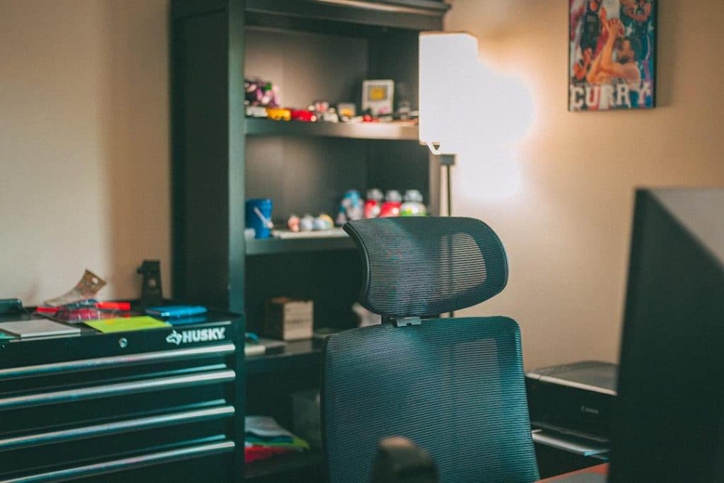 Mesh office chair in home office with shelves and lamp under warm lighting