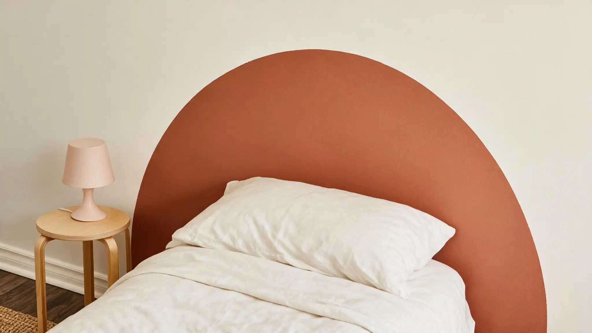 A neatly made bed with white bedding sits against a large terracotta arched headboard, beside a wooden table and lamp.