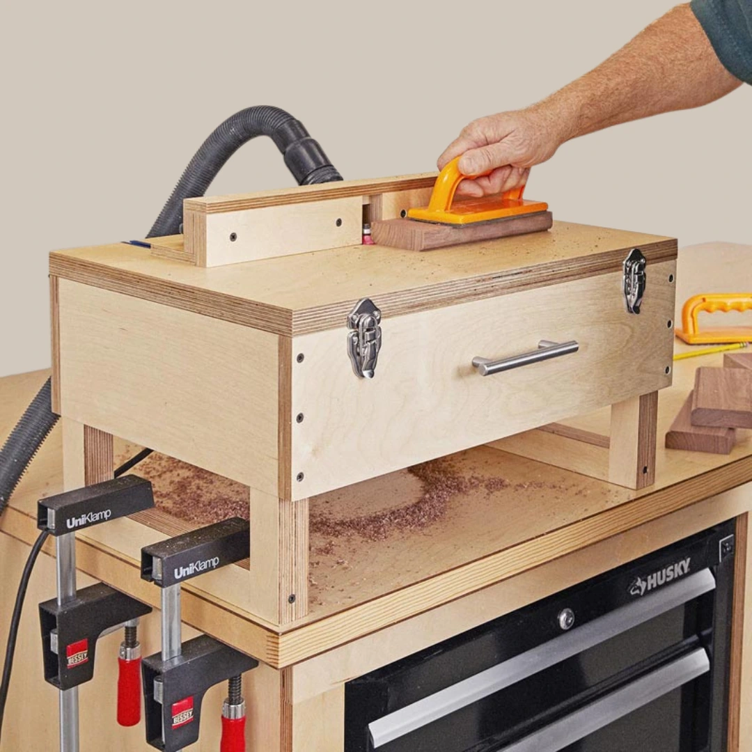 Woodworker guides a wood piece across a homemade router table with a fence, push block, dust hose, and clamped base for control.