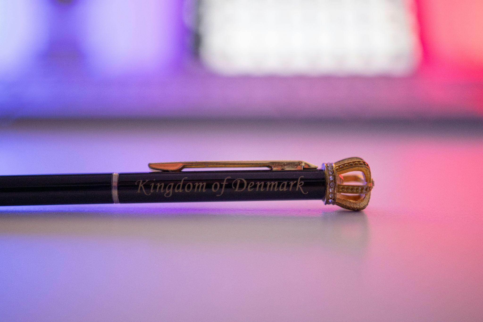 Black pen with gold crown cap on white surface in colorful lighting setting