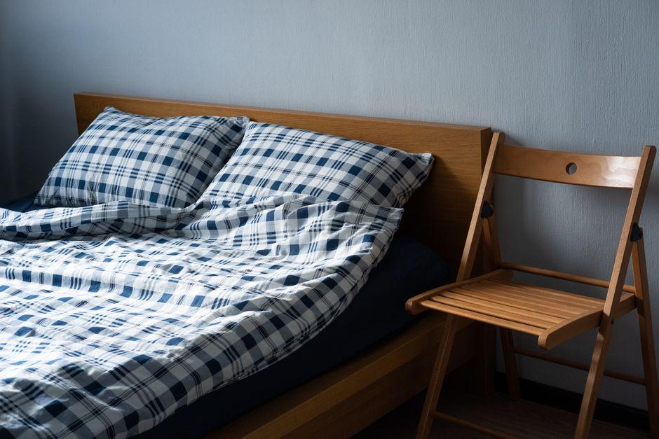 Wooden bed with blue plaid bedding and a folded chair in a softly lit bedroom