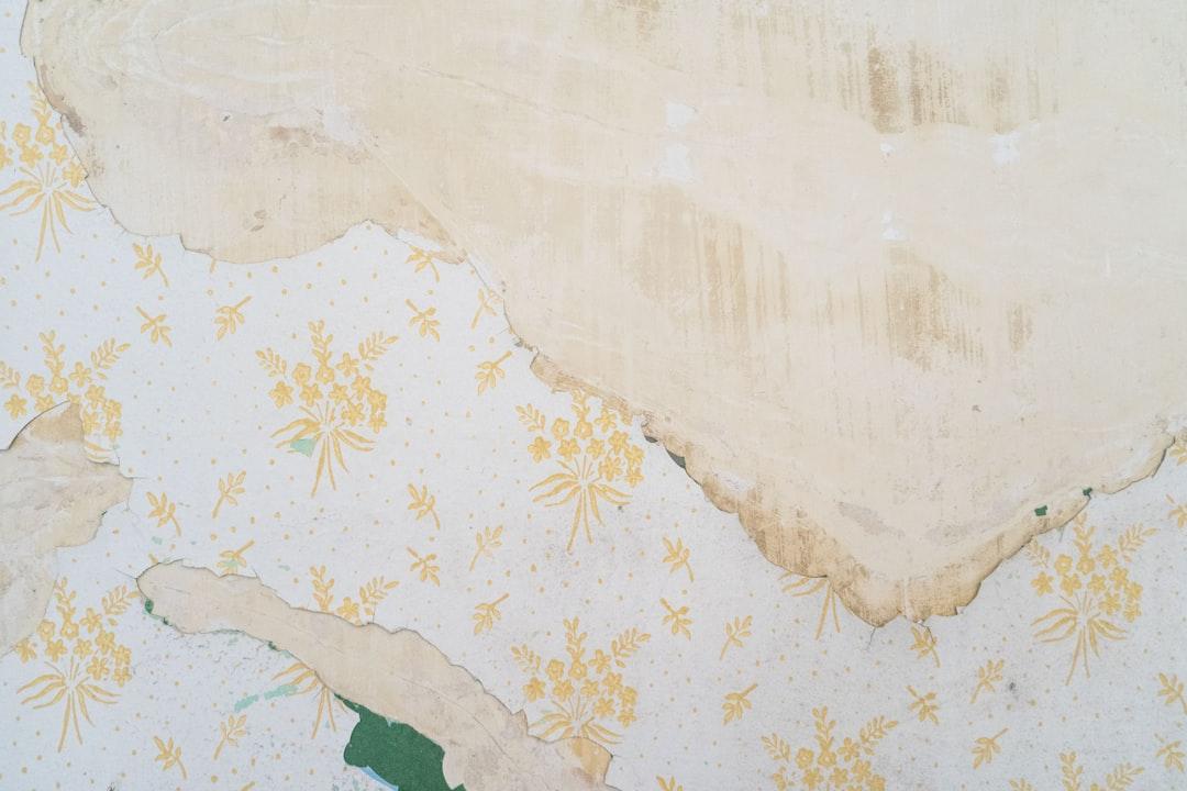 Peeling wallpaper with yellow floral pattern on faded plastered wall