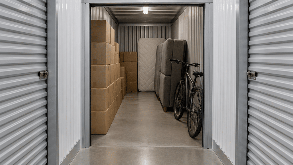 Storage unit with stacked cardboard boxes, a bicycle, and furniture against metal walls