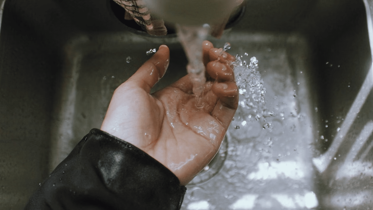 Hand catching water under faucet in stainless steel sink